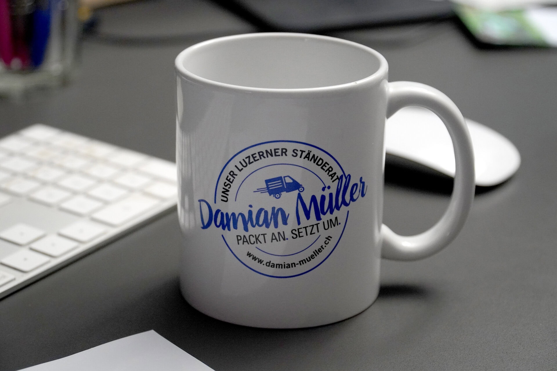 Tasse mit Damian Müller Logo auf Schreibtisch.
